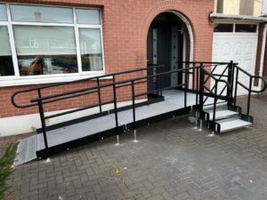 Black modular ramp and step unit installed at the front of a house with red brinks and white windows